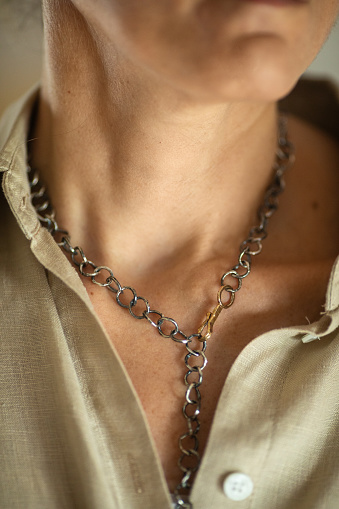 Mature adult woman is designer and artist of unique jewelry made of precious metal. She wearing necklace of gold and silver that she designed and made herself