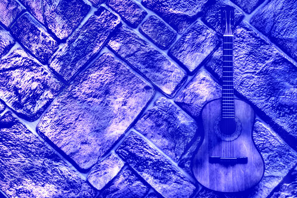 Silhouette of a guitarist holding his guitar on stage. He is in the dark and the guitar is spot lit
