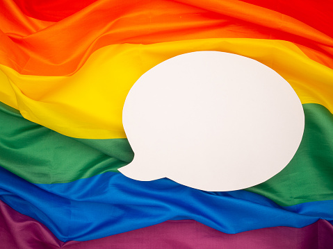 Top view of rainbow flag or LGBT flag with a blank white speech bubble. Close-up photo. Space for text