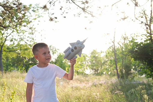 Little boy running with a toy rocket in a sunset field of summer nature. Children's big dream, flight, astronaut, space, success leader winner concept