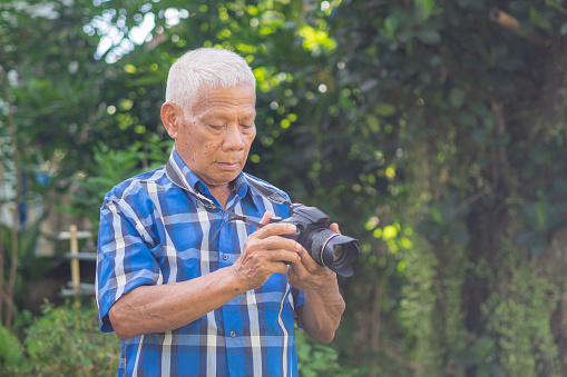 Portrait of a senior man taking photos with a digital camera in the garden.