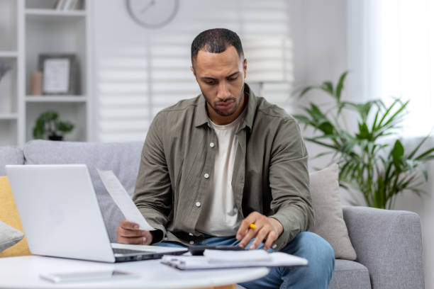 istock Latin American man is focused working remotely at home on a laptop and with documents 1665396076
