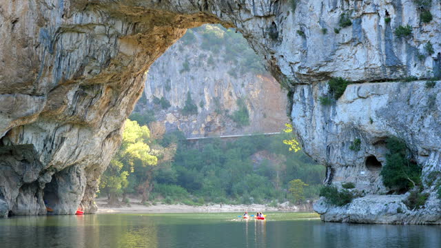 Kayaks swimming through the famous Pont d'Arc in France while water drops from the ceiling and birds fly around