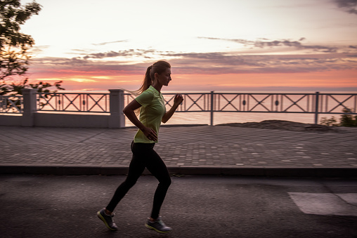 Young woman in sportswear runs along the path at dawn. Morning routine, meditation, feeling of freedom. Girl is wearing black leggings and a yellow T-shirt. Beautiful red sky. Concentrated motivation