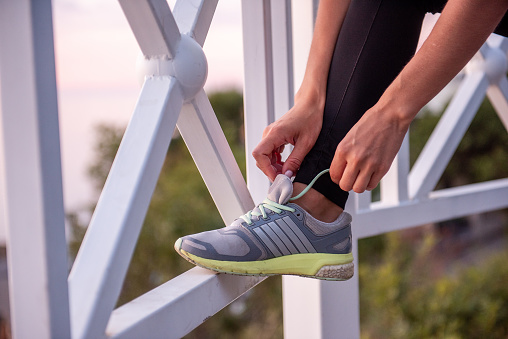 Young woman athlete tying shoelaces on sneakers on pavement at sunrise. Break fitness workout, morning routine. Closeup sporty portrait of caucasian girl. Sportswoman before start workout. Copy space