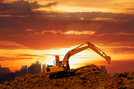 Excavators  are digging the soil in the construction site on the  sunset sky background
