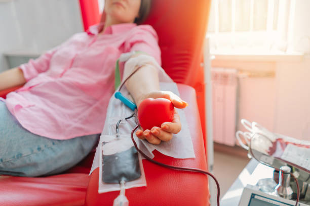 Young woman making blood donation in hospital. Young woman making blood donation in hospital. A woman donates blood while holding a red heart. Blood donation. blood bank stock pictures, royalty-free photos & images