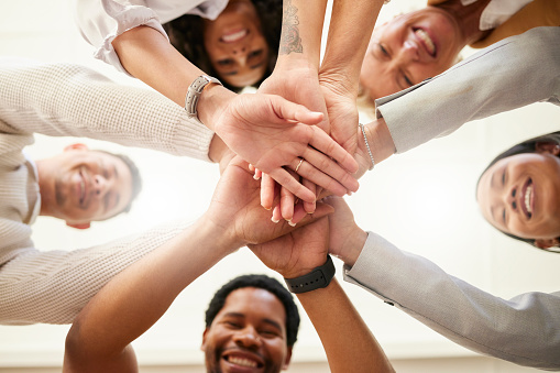Office, team building and hands together from below in huddle for teamwork, collaboration and motivation at startup. Work, goals and diversity, group of people with business growth and staff support.
