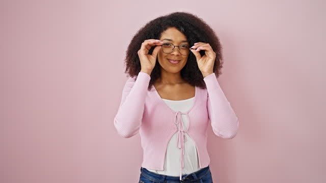 African american woman smiling confident taking out glasses over isolated pink background