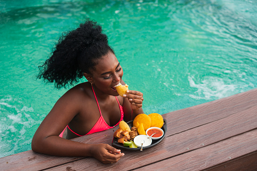 Afro-Colombian woman of Latino ethnicity between the ages of 20-30 is eating in the pool of a rooftop of a hotel in Cartagena