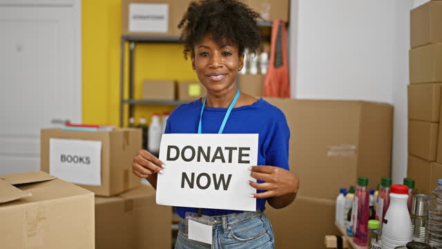 African american woman volunteer holding donate now message at charity center