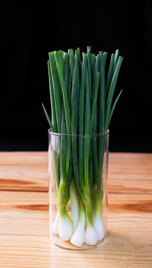 Spring onions that have been cleaned and are ready to eat are stored in glass jars on a wooden table against a black background.