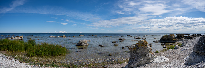 In this expansive panoramic capture, the vividly colored stones of Fårö's beach serve as a striking foreground, providing a textural contrast to the wide stretch of ocean that lies beyond. The frame extends horizontally to encompass a sweeping view of the sea, meeting the sky at a distant horizon. The broad scope of the panorama emphasizes the vastness and serenity of the natural landscape, creating a visually compelling composition that highlights both the intricate details of the rocky shore and the boundless beauty of the maritime horizon.