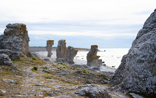 In this evocative landscape, the Langhammars raukarea occupies a prominent position on a beach in Gotland. This area, known for its distinctive rock formations or 'rauks,' offers a geological spectacle against the backdrop of a sprawling seascape. The craggy, weathered forms of the rauks serve as natural sculptures, each one unique and shaped by the forces of time and nature. Their imposing presence adds a sense of grandeur and mystique to the beach setting, contrasting with the fluid and ever-changing backdrop of the ocean and sky. This scene captures the essence of Gotland's unique coastal environment, blending geological wonder with maritime beauty in a compelling visual narrative.