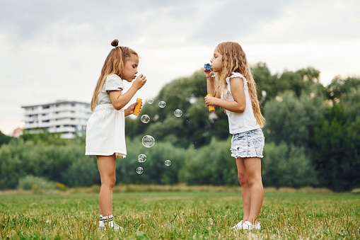 Bunch of bubbles. Two girls are playing together on the green field.