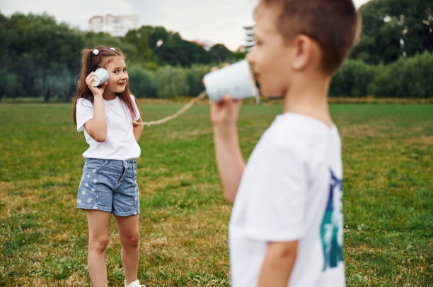 Talking by using string can phone. Boy and girl are together having fun on the field at daytime