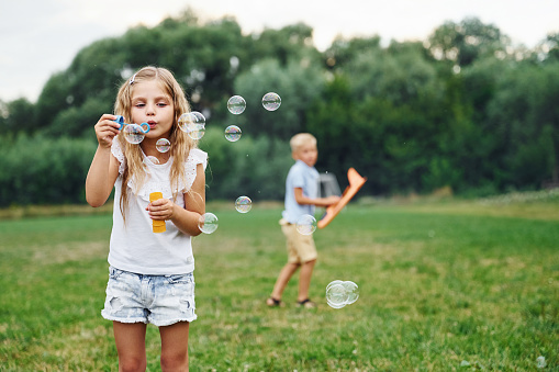 Little girl is playing with bubbles, boy is holding toy plane behind.