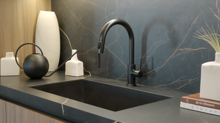 Angle view of integrated sink and black faucet with button for switching modes. Matte surface from black marble with golden pattern. Kitchen cabinetry with items for decor