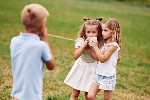 istock Talking, using string can toy. Kids are having fun on the field at daytime together 1665580026