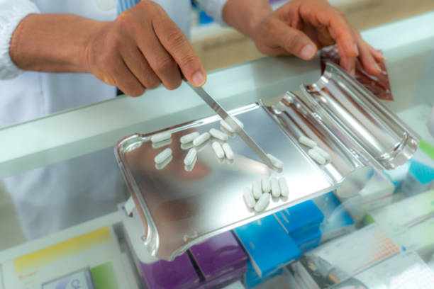 istock Unreconized male with white lab coat transferring while counting a number of pills on stainless tray, he is preparing drug pack to patient in the pharmacy drugstore. Medicine, pharmaceutics, health care. 1665586572