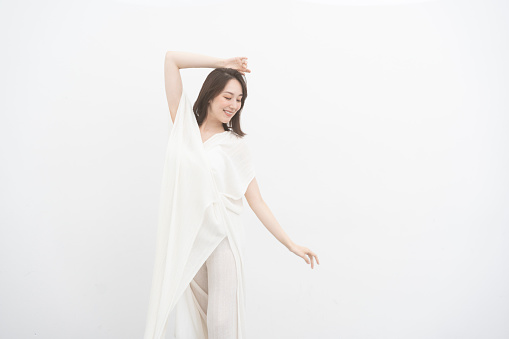 A woman wearing a white dress is dancing. Beauty portrait of a beautiful Japanese woman/white background studio shot/wearing white clothes.