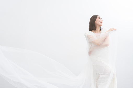 A woman wearing a white dress is dancing with a veil.Beauty portrait of a beautiful Japanese woman/white background studio shot/wearing white clothes.