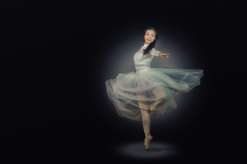 Beautiful Young Asian Ballerina Spinning Gracefully in the Spotlight. She is dressed in a white airy dress and a modern tutu.