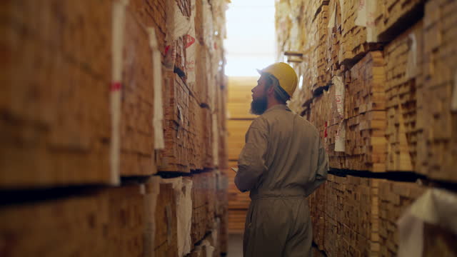 Worker at a wood plant checks stock in a wood shed.