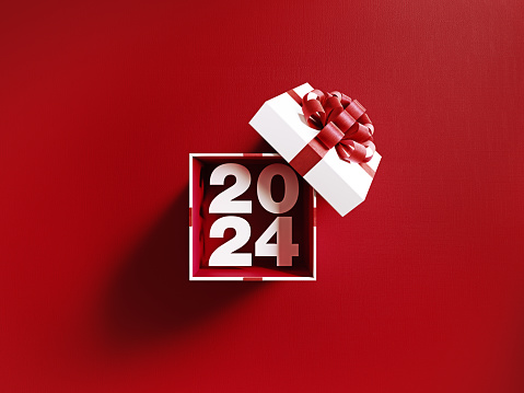 2024 is coming out of a white gift box tied with red ribbon on red background. Horizontal composition with copy space. Directly above. Great use for Christmas related gift concepts.