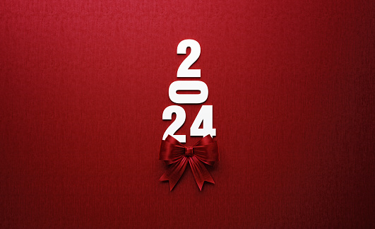 2024 text forming a Christmas tree and is tied with red ribbon on red background. Horizontal composition with copy space. Directly above. Great use for Christmas and 2024 concepts.