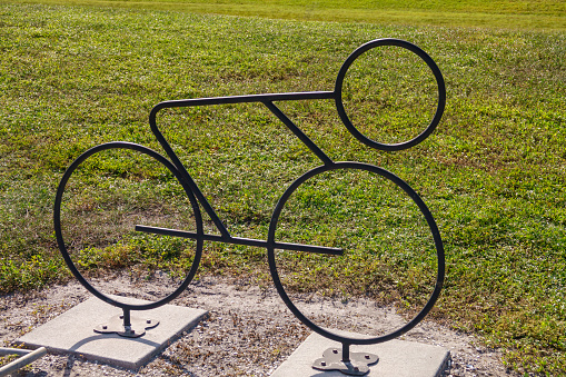 Silhouette of a decorative bike rack, shaped like a bicycle and bolted to concrete pads in a public park, for motifs of minimalism and functionality, simplicity and street art