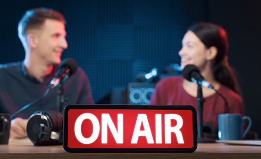 Young radio hosts working in the studio, On Air sign in the foreground