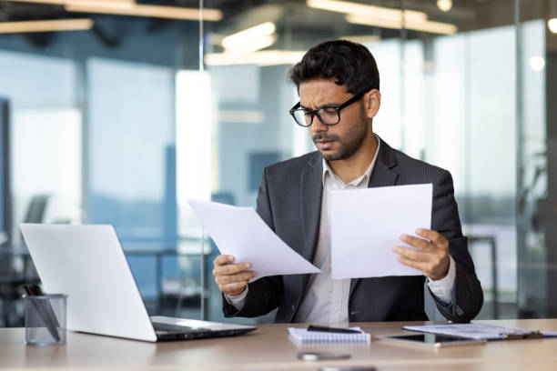 istock Serious concentrated businessman inside office behind paper work, financier reading and checking reports holding in hands, man thinking about technical solutions at workplace 1665704772