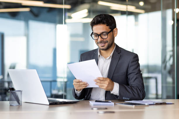 istock Experienced young financier at workplace checking and reading company financial report, businessman behind paper work inside office, satisfied with achievement results 1665704785