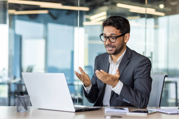istock Young successful hispanic businessman talking on video call using laptop, man inside office at workplace, online meeting with colleagues and partners 1665704792