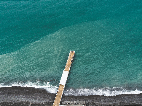 Aerial shot of jetty extending over blue water