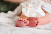 Baby feet. Infant feet. Cute little sleeping and lying on the bed at home. Closeup. Tiny bare feet of newborn baby girl or boy wrapped in a soft, and cozy blanket. Side view.