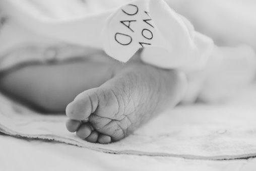 Baby feet. Infant feet. Cute little sleeping and lying on the bed at home. Closeup. Tiny bare feet of newborn baby girl or boy wrapped in a soft, and blanket. Side view. Black and white photo. Dad mom