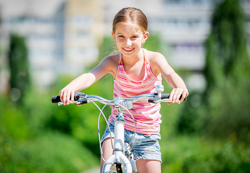 smiling little girl riding bicycle with green park on the background