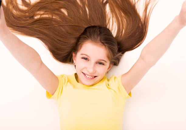 Happy little girl smiling at camera on a sunny day isolated outdoors green grass external walls of the house on the background. The child looks calm, gentle, natural.