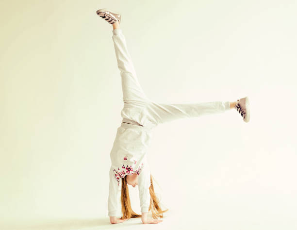 Active little girl in grey sport clothes doing a handstand on white background