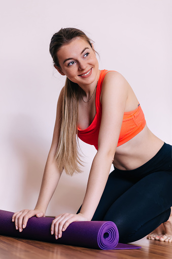 Young attractive woman with yoga mat indoors, preparing for exercise, unrolling or rolling yoga mat.