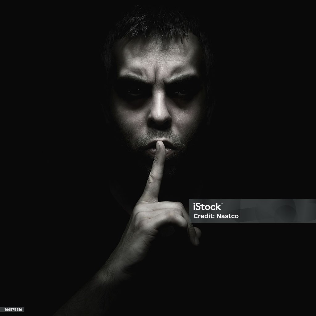 A man telling someone to be silent Evil man gesturing silence, quiet isolated on black background Finger on Lips Stock Photo