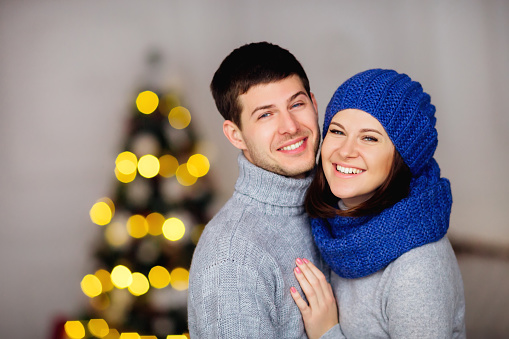 couple in love smiles in winter clothes on the background of blurred Christmas tree.