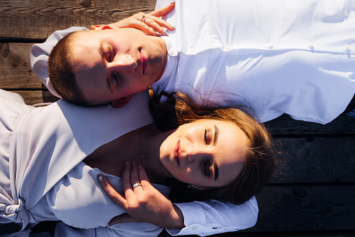 a woman and her husband lie on the wooden surface with closed eyes while sunlight shines on them