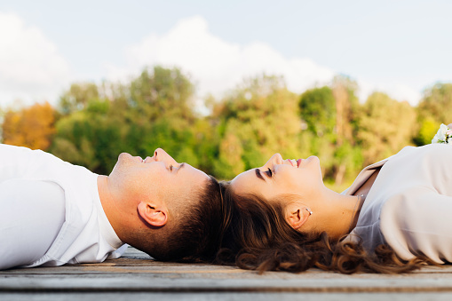 A man and a woman lie on the wooden surface a head to head and smile on the background of nature