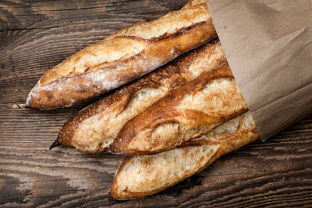 Baguettes bread Four baguette bread loaves in paper bag on wooden background bread bakery baguette french culture stock pictures, royalty-free photos & images