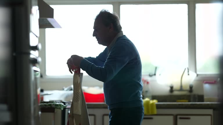 Senior chef removing apron after food preparation. Retired older man takes off apron finishing meal routine, candid and authentic lifestyle