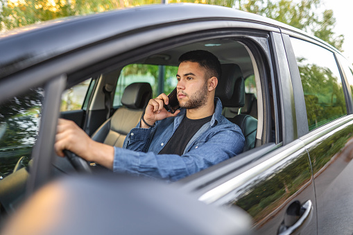 Young man talking on a phone call while driving car