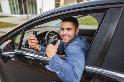 Portrait of a young man holding his new car keys while sitting in drivers seat